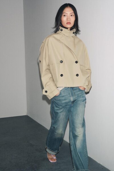 Modelka w krótkim beżowym trenczu Zara i jeansach – kobieta w oversize’owym trenczu w kolorze piaskowym, zestawionym z szerokimi dżinsami w stylu vintage. Stylizacja utrzymana w klimacie casual chic z nutą nonszalancji.