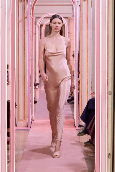 Satynowa slip dress – Długa, pastelowa suknia na cienkich ramiączkach, o kroju slip dress z delikatnym dekoltem typu cowl neck. Lśniąca satyna układa się miękko na sylwetce, nadając lookowi subtelnej zmysłowości i intymnego wyrafinowania.