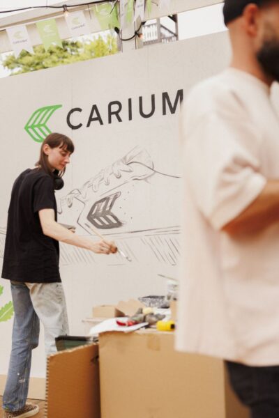 Artystka maluje mural z logotypem Cariuma i szkicem sneakersa podczas premiery marki w Polsce. Event połączył sztukę uliczną, skateboarding i kulturę miejską.