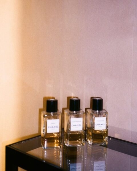 Kompilacja trzech flakonów perfum Chanel o bursztynowym odcieniu, stojących na szklanej powierzchni. W minimalistycznej, luksusowej scenerii, idealne ujęcie do opisu zapachów Chanel.