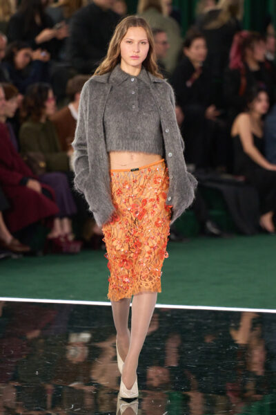 Modelka na wybiegu Gucci jesień 2025 – ubrana w oversize’ową marynarkę w intensywnym odcieniu pomarańczu, zestawioną z luźnymi spodniami o szerokich nogawkach w tym samym kolorze. Stylizacja odwołuje się do estetyki power dressing, z nutą retro glamour charakterystyczną dla domu mody Gucci.