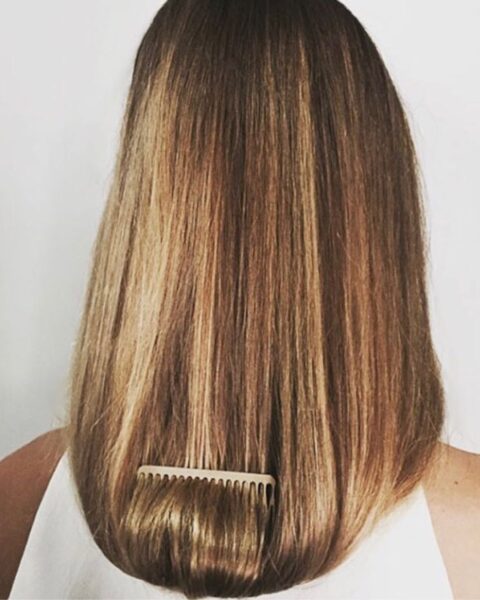 Zdjęcie kobiety stojącej tyłem. Ma ciemnoblond włosy, rozpuszczone i wpięty w nie grzebień. Jest ubrana w biały top.