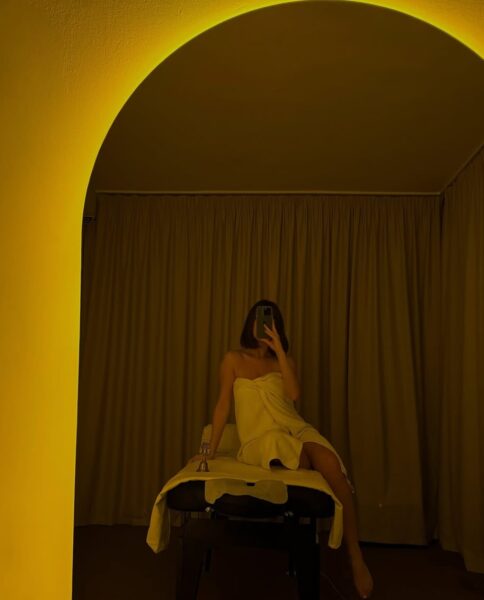 Osoba owinięta ręcznikiem siedząca na stole do masażu w nastrojowym, żółtym oświetleniu gabinetu spa