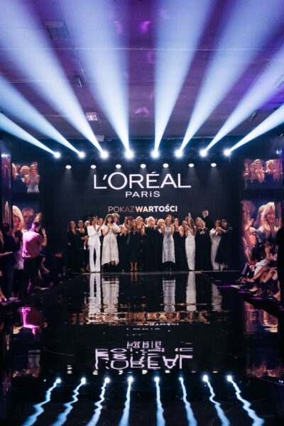 Finał „Pokazu Wartości” L’Oréal Paris – wszystkie modelki, ambasadorki i uczestniczki stoją razem na scenie, oklaskiwane przez publiczność, w świetle reflektorów i logotypu marki na tle.