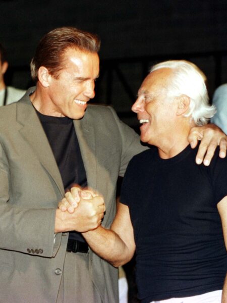 Arnold Schwarzenegger i Giorgio Armani – ujęcie zza kulis, pokazujące przyjacielskie spotkanie projektanta z gwiazdorem kina akcji i jego ówczesną partnerką, Marią Shriver. Armani uśmiechnięty w czarnym T-shircie, w centrum uwagi i otoczony ikonami popkultury lat 90.