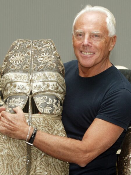 Giorgio Armani w pracowni haute couture – projektant pozuje przy manekinie ubranym w bogato zdobioną kreację, otoczony misternie wykonanymi strojami, które łączą tradycję rzemiosła i luksusową nowoczesność.