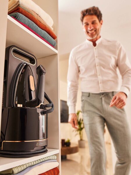 Mężczyzna idący w kierunku półki z ubraniami i generatorem pary Braun CareStyle 9 Pro.