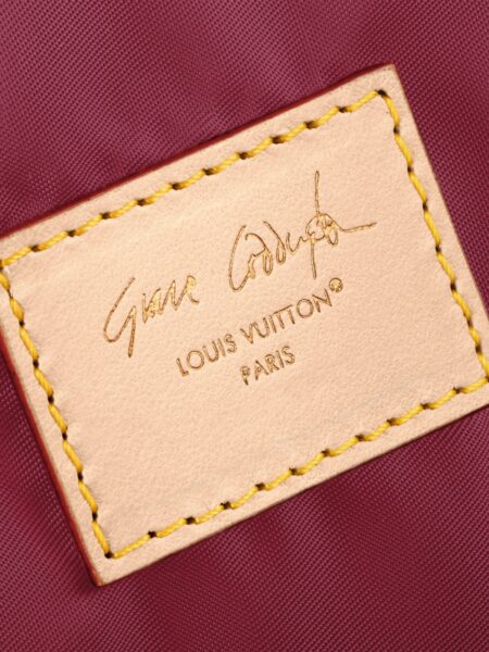 Louis Vuitton z Grace Coddington: zbliżenie na skórzaną metkę z widocznym podpisem artysty Graya Godlewski; beżowa skóra z żółtym przeszyciem kontrastuje z bordową podszewką, podkreślając rzemieślnicze wykończenie i ekskluzywny charakter projektu.