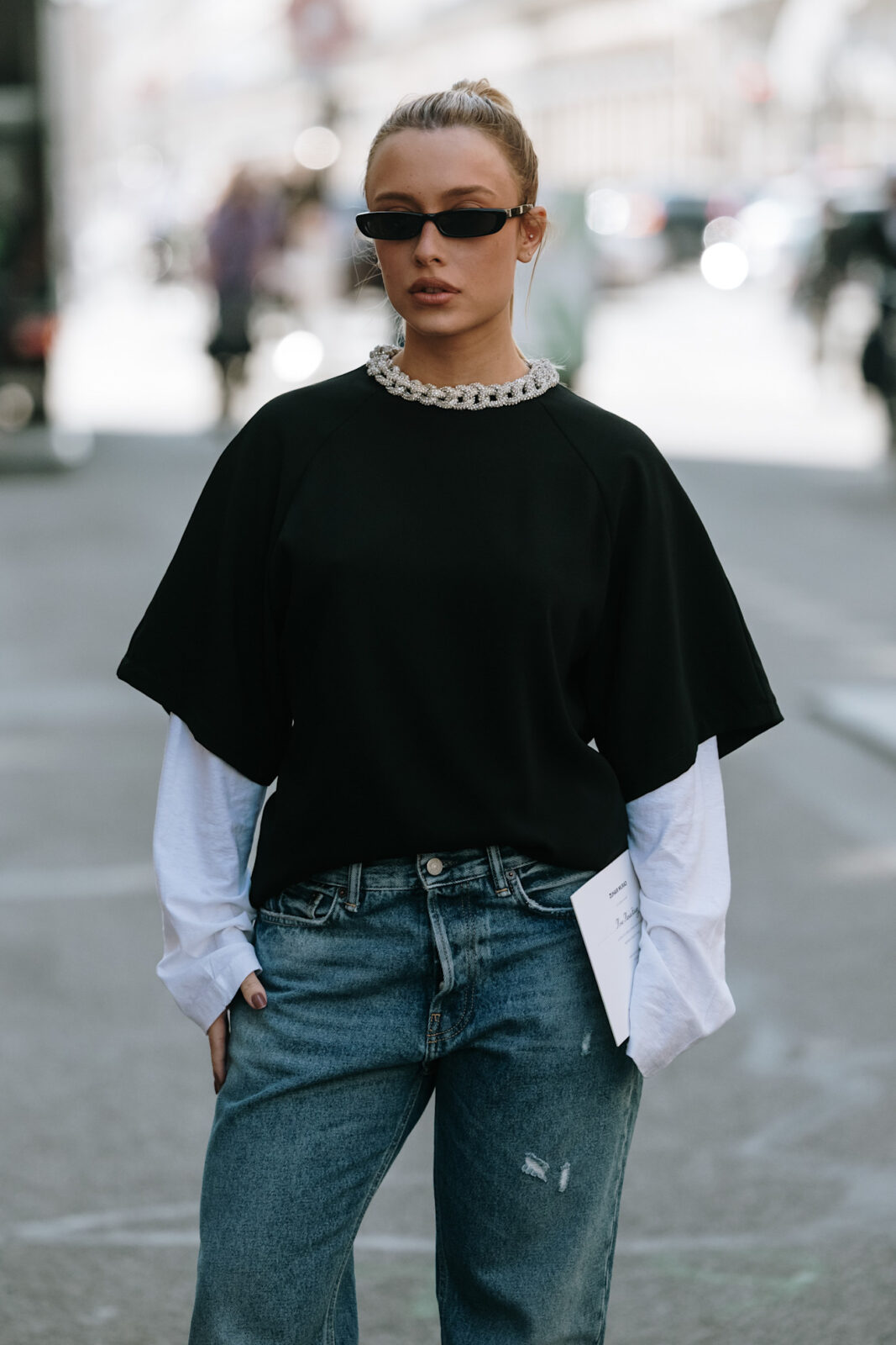 Najlepsze marki streetwear 2025: Kobieta w czarnym tshircie i czarnych okularach pozująca na ulicy.