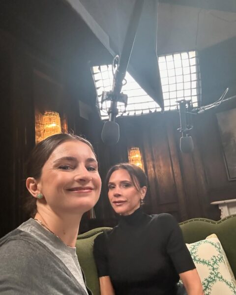 Chloe Malle robi selfie z Victorią Beckham podczas nagrania odcinka podcastu The Run-Through with Vogue. Obydwie siedzą na zielonej sofie w eleganckim wnętrzu. Chloe uśmiecha się subtelnie, ubrana w szarą bluzę, a Victoria w czarnym golfie patrzy w stronę obiektywu.