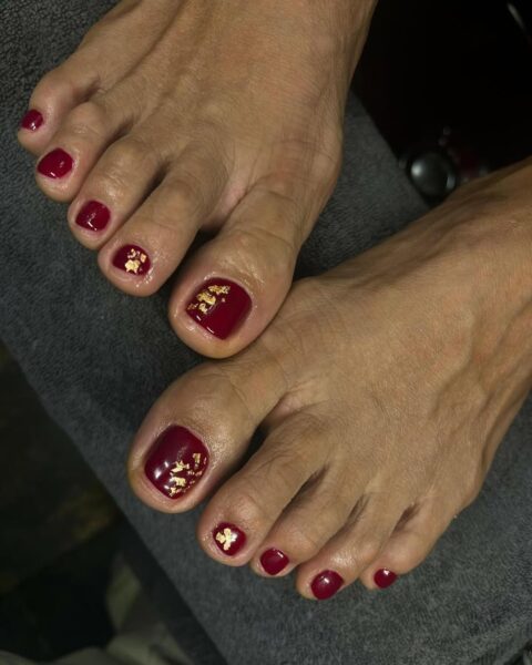 Klasyczny bordowy pedicure ze złotymi płatkami na dużych paznokciach – ponadczasowe połączenie, które łączy głębię czerwieni z luksusowym, biżuteryjnym detalem.