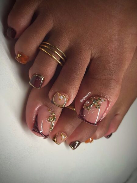 Pedicure w brązach i burgundzie z bogatymi zdobieniami 3D – złotymi liniami, perełkami i mikrozłoceniami – efektowna, biżuteryjna stylizacja w klimacie haute couture, przyciągająca uwagę i idealna na wyjątkowe okazje.