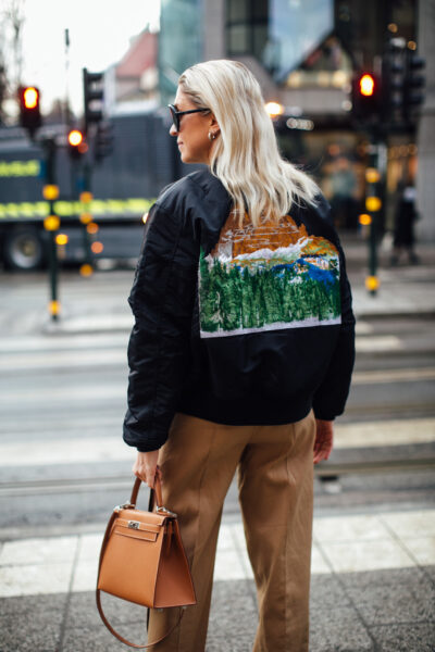 Hailey Bieber w czarnej, oversize’owej bomberce skórzanej, czarnych sportowych szortach i z włosami upiętymi w gładki kok, sfotografowana nocą na ulicach Nowego Jorku.