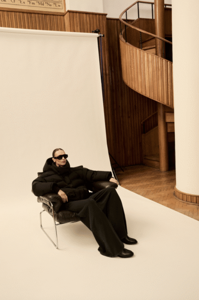 Modelka w oversize’owej, czarnej pikowanej kurtce z mocno zaznaczonymi ramionami, szerokich spodniach i masywnych butach. Całość dopełniają okulary przeciwsłoneczne XXL. Look futurystyczny, inspirowany estetyką athleisure i haute couture.