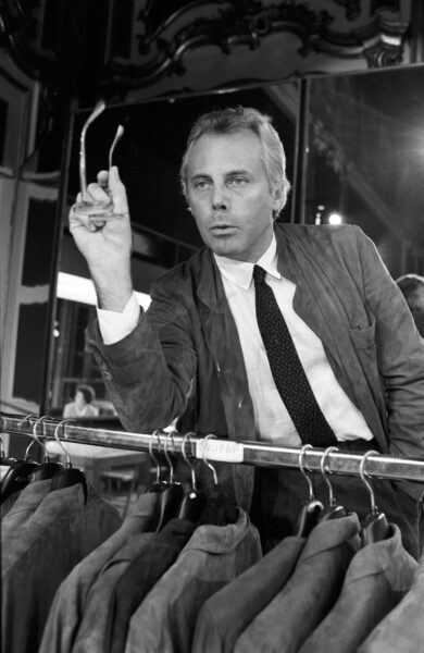 Giorgio Armani filmy: Młody Giorgio Armani przy pracy – czarno-biała fotografia przedstawiająca projektanta w latach 70., analizującego projekty marynarek w swojej pracowni. Ujęcie ukazuje skupienie i perfekcjonizm, które zdefiniowały jego karierę.