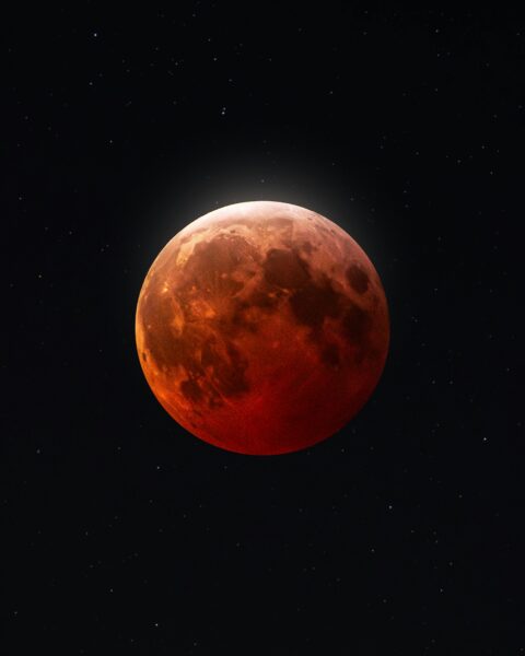 Krwawy Księżyc podczas zaćmienia na tle czarnego nocnego nieba pełnego gwiazd.