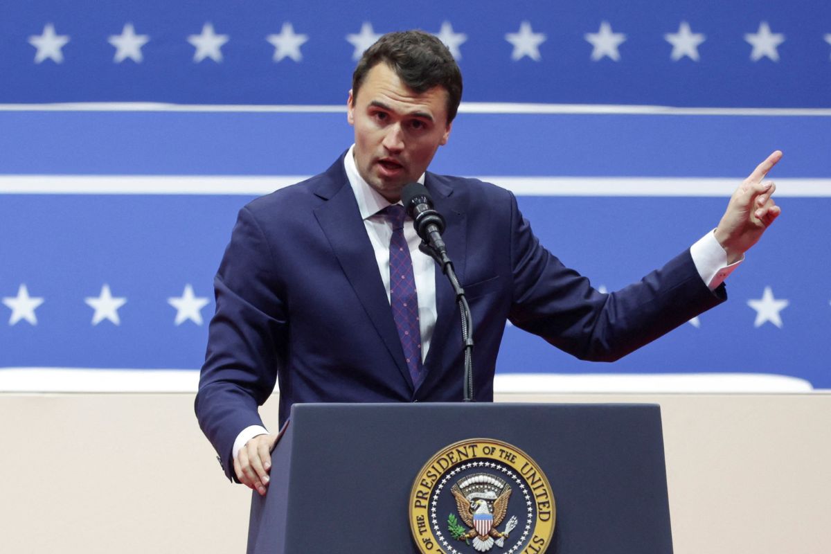 Mężczyzna w garniturze przemawia przy mównicy z symbolem prezydenckim na tle niebieskiej scenografii.