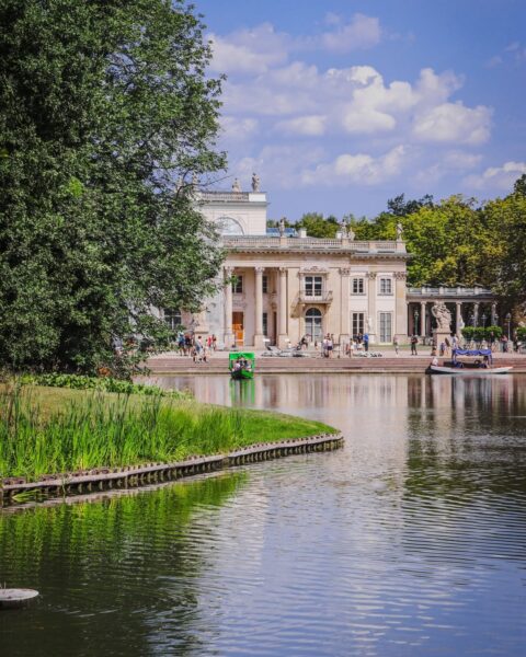 Pałac na Wyspie w Łazienkach Królewskich w Warszawie, widok od strony stawu z łodziami i spacerującymi turystami w słoneczny dzień
