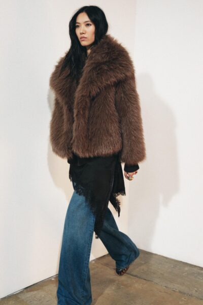 Modelka w obszernym futrze w odcieniu gorzkiej czekolady, jeansach typu flare i czarnej sukience z koronkowym wykończeniem. Stylizacja łączy nonszalancję z elegancją boho.