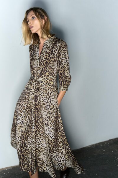 Modelka w sukience midi w cętkowany, panterkowy wzór, z lekko rozkloszowanym dołem i rękawami ¾. Stylizacja emanuje zmysłową elegancją w duchu współczesnej kobiecości.