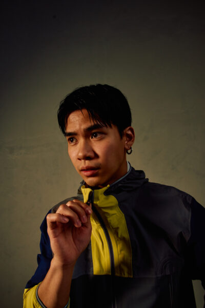 Portret mężczyzny w sportowej kurtce Under Armour w odcieniach granatu i żółci. Model zapięty pod szyję, o intensywnym spojrzeniu, uchwycony w miękkim świetle, które podkreśla jego skupienie i energię treningu.