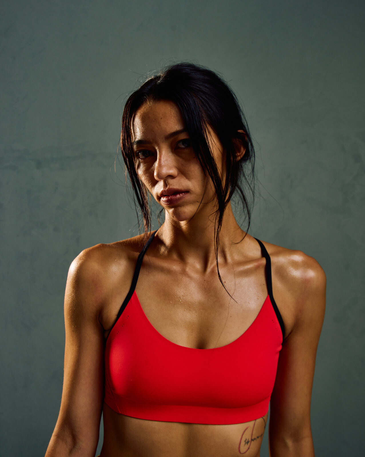 Under Armour nowa kolekcja: Kobieta w neonowo-pomarańczowym staniku pozuje w sportowym wydaniu na tle szarej ściany.