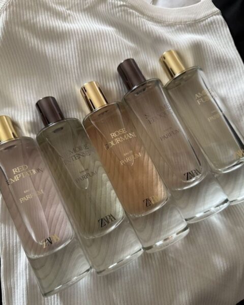 Bursztynowe perfumy z Zary: Pięć butelek wody perfumowanej Zara leżących na białym prążkowanym topie. Widoczne flakony to od lewej: Red Temptation, Memoire Intense, Rose Gourmand, Sublime Époque oraz Amber Fusion. Każda butelka ma złotą lub brązową nakrętkę i jasną, beżowo-branszową zawartość.