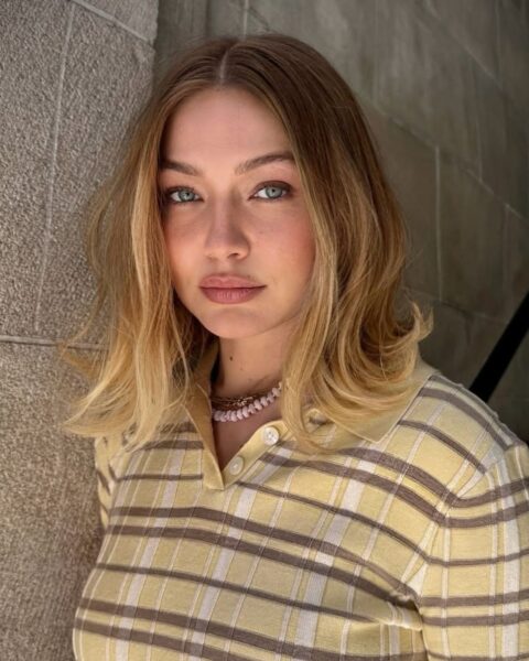 Gigi Hadid w sweterku polo w kratę i z krótkim, falowanym blond bobem. Inspiracja, jak dobrać fryzurę do kształtu twarzy, by wyglądała świeżo i nowocześnie.