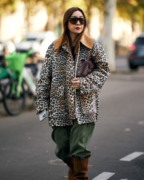 Street style: kobieta w efektownej, jesiennej stylizacji. Ma na sobie krótką, luźną kurtkę w panterkę z futrzanym kołnierzem, którą połączyła z szerokimi, zielonymi spodniami cargo i wysokimi, zamszowymi kozakami w kolorze brązowym. Całość uzupełniają duże okulary przeciwsłoneczne i torebka z monogramem.