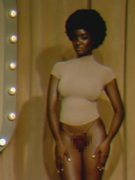 Portret kobiety w podobnej stylizacji retro – cieliste body i fryzura afro, na tle teatralnej kurtyny z żarówkami po bokach; kadr stylizowany na wczesne programy telewizyjne z lat 70., z lekkim ziarnem i ciepłym oświetleniem.