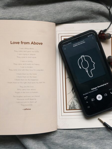 7 gatunków audiobooków: Książka a na niej telefon ze słuchawkami podłączonymi do audiobooka.