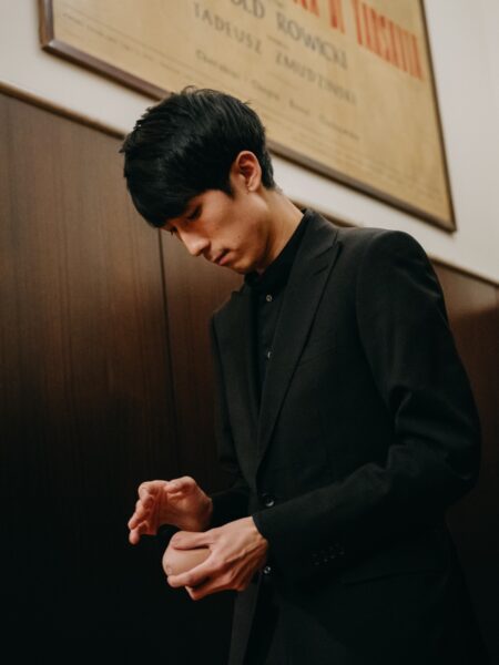 Eric Lu w korytarzu Filharmonii Narodowej, skupiony tuż po zejściu ze sceny. W czarnym garniturze, z dłonią opartą o drugą, wygląda na zamyślonego – to moment wyciszenia po emocjonalnym finale.