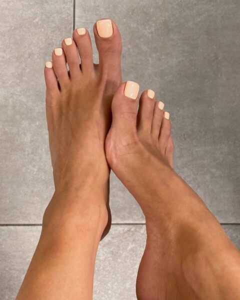 Letni, minimalistyczny pedicure w modnym odcieniu jasnej brzoskwini lub morelowego nude (pastelowy pomarańcz). Lśniący kolor doskonale podkreśla opaloną skórę i elegancję stóp, stanowiąc subtelny, ale wyrazisty dodatek do casualowej stylizacji z dżinsami.