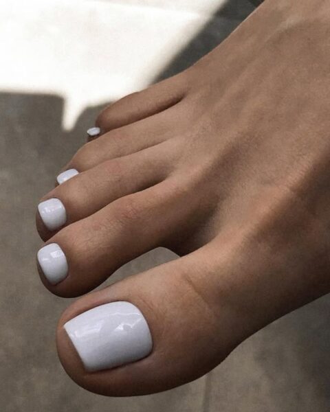 Nowoczesny, lśniący pedicure w kolorze czystej, idealnej bieli (nawiązującej do bieli polarnej lub chmur). Ten minimalistyczny, ale wyrazisty trend doskonale podkreśla opaloną skórę i symbolizuje elegancję w stylu clean girl.
