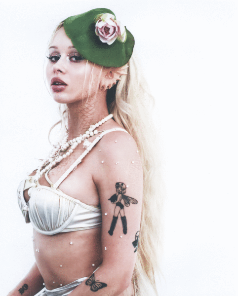 „Aktivist" Lila Janowska: Kobieta o długich, jasnych włosach w artystycznym portrecie stylizowanym na wodną istotę; ma na sobie metaliczny gorset z perłami, ozdobę z liścia lilii wodnej i różowego kwiatu na głowie oraz delikatne perły na ciele i twarzy, tworzące efekt morskiej syreny.