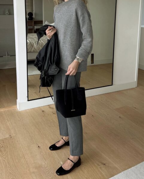 Fashion girl w klasycznej, minimalistycznej odsłonie. Szary, luźny sweter i szare spodnie o długości 7/8. Elementy garderoby, które budują status fashion girl: aksamitna czarna torebka, lakierowane baleriny i zestaw srebrnej biżuterii, podkreślające elegancję.