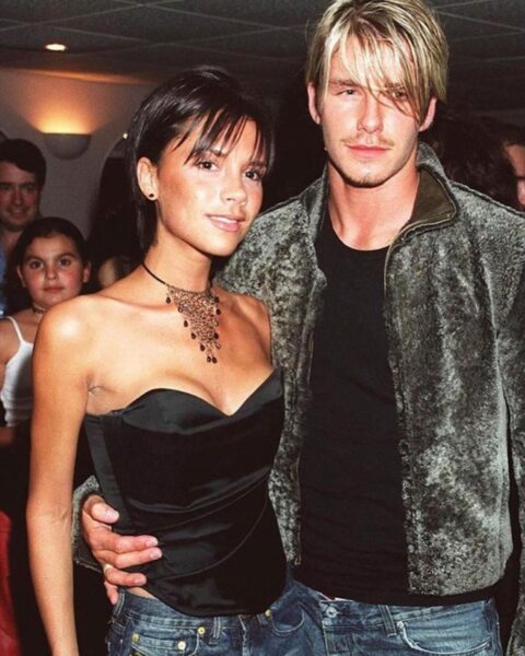 Pierścionki zaręczynowe Victoria Beckham: Młoda Victoria Beckham pozująca z Davidem Beckhamem w latach 90., w krótkiej fryzurze pixie cut, z pierwszym subtelnym pierścionkiem zaręczynowym widocznym na dłoni.