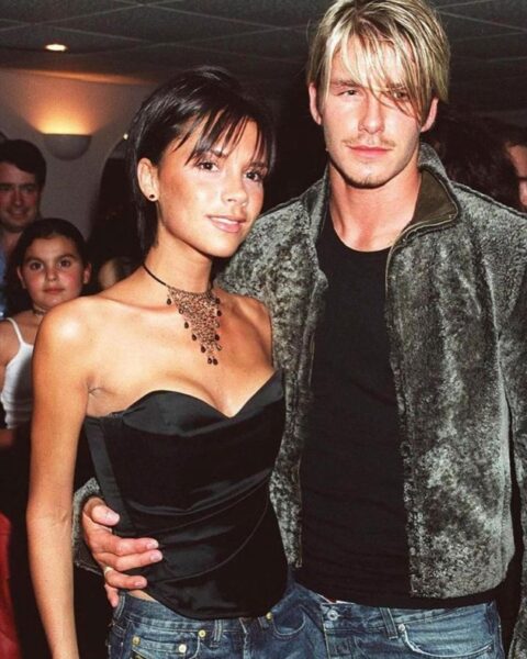 Młoda Victoria Beckham pozująca z Davidem Beckhamem w latach 90., w krótkiej fryzurze pixie cut, z pierwszym subtelnym pierścionkiem zaręczynowym widocznym na dłoni.
