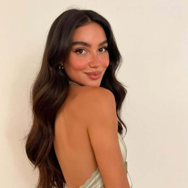 Miodowa opalenizna przez całą zimę. ortret uśmiechniętej młodej kobiety z długimi, ciemnymi włosami, ubranej w jasnozieloną sukienkę typu halter, odwracającej się przez ramię i prezentującej swoją twarz z piegami oraz piękną opalenizną.