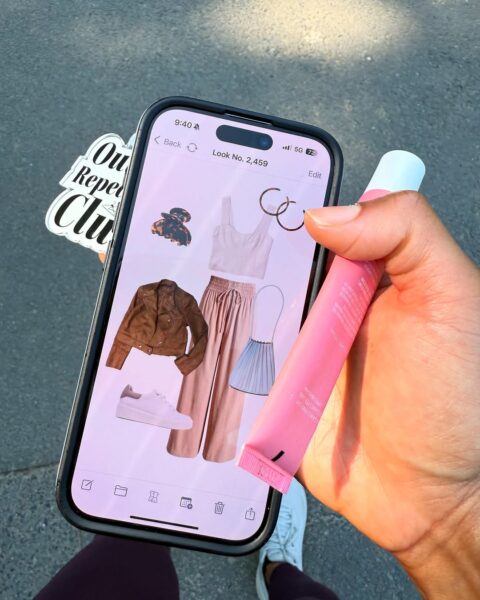 Zbliżenie na ekran smartfona, na którym wyświetla się cyfrowa stylizacja nr 2459, stworzona w mobilnej aplikacji. Look ten, złożony z brązowej kurtki i różowego kompletu, jest świetnym przykładem, co można uzyskać dzięki najlepszym aplikacjom do organizacji szafy. Użytkowniczka trzyma telefon, planując strój na dany dzień.