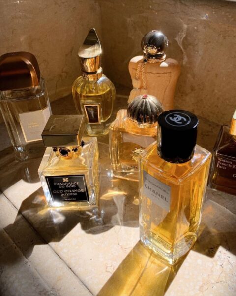 Zgrupowanie ekskluzywnych flakonów perfum niszowych i luksusowych, w tym Chanel Coromandel, Fragrance Du Bois Oud Orange Intense, Guerlain Cuir Beluga, Montale oraz Maison Francis Kurkdjian Grand Soir, ułożonych na marmurowej powierzchni, częściowo oświetlonej ciepłym, słonecznym światłem. Widoczne są różnorodne kształty i zdobienia flakonów, podkreślające ich unikalność i kunszt wykonania.