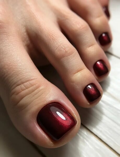 Zbliżenie na klasyczny pedicure w kolorze głębokiego bordo o metalicznym połysku. Lustrzany efekt i perfekcyjnie wypolerowana płytka paznokcia podkreślają elegancki, wieczorowy charakter stylizacji.