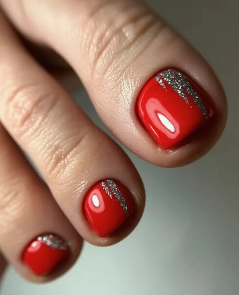 Subtelny pedicure w czerwonym kolorze z delikatnymi srebrnymi zdobieniami przy nasadzie paznokci. Geometryczny akcent dodaje nowoczesności i świetnie komponuje się z połyskującym wykończeniem lakieru.