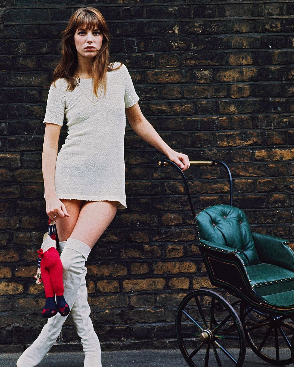 Jane Birkin w białej sukience mini i białych kozakach, oparta o wózek dziecięcy. ikony stylu które nigdy nie miały stylisty