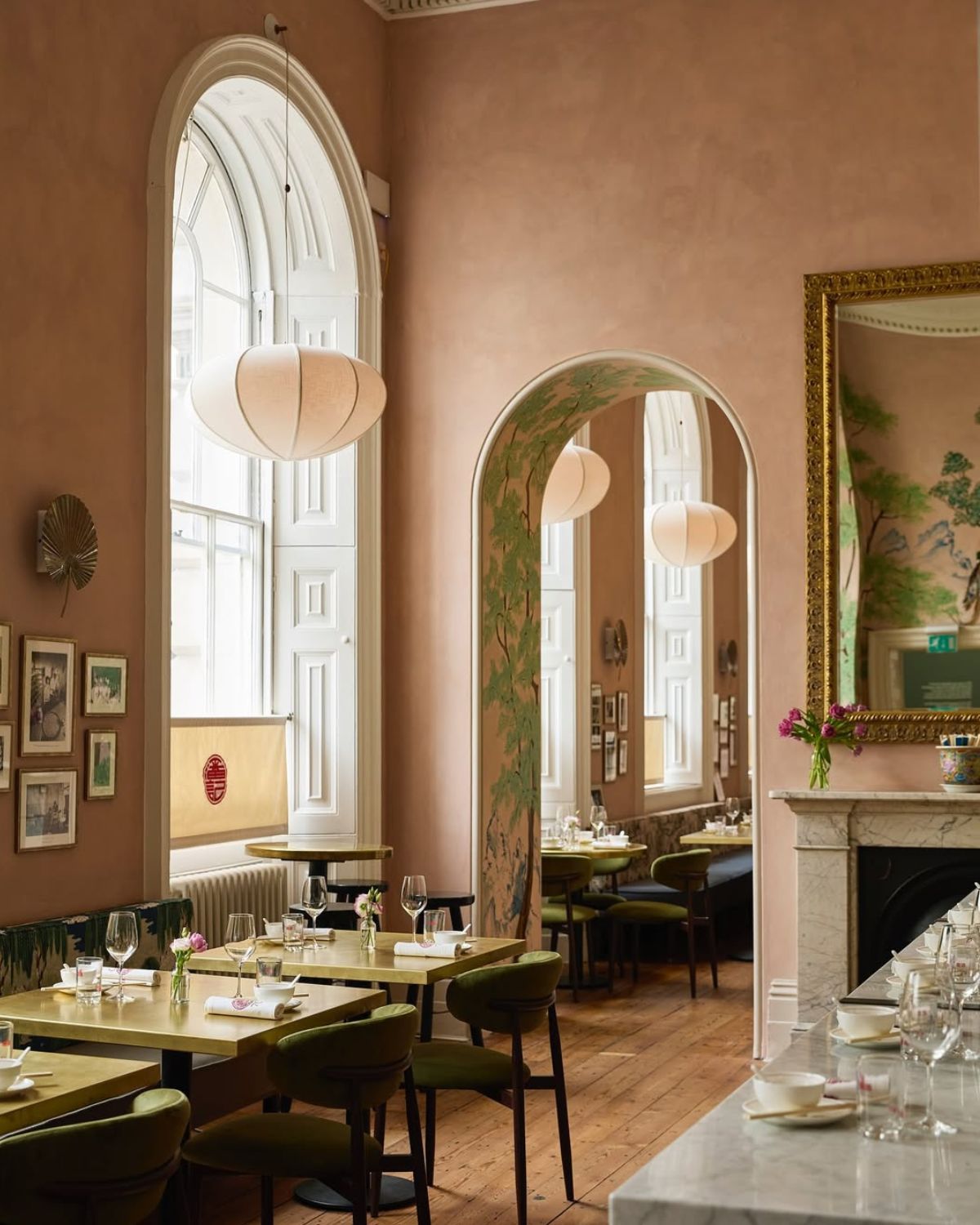 Wnętrze eleganckiej restauracji w pastelowym różu i oliwkowej zieleni, z wysokimi oknami i marmurowym barem, emanujące szykiem w stylu chinoiserie. Idealna sceneria na ogłoszenie zwycięzców Kulinarnych Oscarów 2025 - luksusowy wystrój jako inspiracja dla kobiet ceniących klasę i piękno.