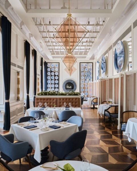 Symetryczne, bardzo eleganckie wnętrze luksusowej restauracji z wysokim sufitem, zdobione długimi, granatowymi aksamitnymi zasłonami, mozaikową podłogą i detalami z porcelany w odcieniach kobaltu i błękitu. Ekskluzywny design i klasa, którą zachwyca restauracja Europejski Grill (Warszawa), to idealna inspiracja dla miłośniczek wyrafinowanego stylu i emocjonalnego piękna wnętrz.