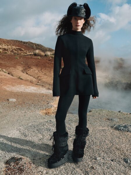 Kobieta o blond włosach w stylizacji typu „old money” – czarna, dopasowana sukienka midi z krótkim rękawem, szeroki pasek w talii i klasyczna torebka. Zdjęcie wykonane w eleganckim wnętrzu garderoby z elementami drewna i szkła.