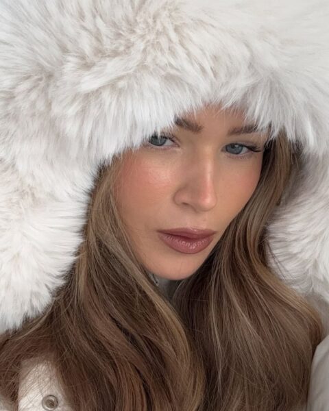 Kobieta w minimalistycznym, sportowym stroju typu athleisure – czarnym crop topie i dopasowanych spodenkach lub legginsach – pozuje do selfie w sypialni. Ma włosy spięte w wysoki, energiczny kucyk i emanuje pewnością siebie. Zdjęcie jest utrzymane w estetyce fitness i wellness, idealne do artykułu o modzie sportowej lub budowaniu poczucia własnej wartości.