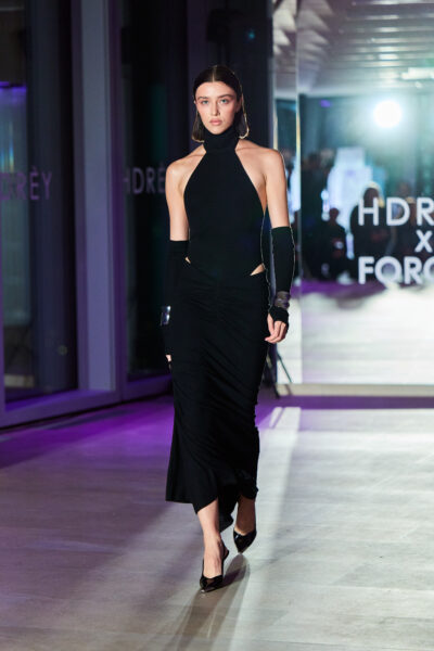Kolejne ujęcie czarnej sukni maxi z odsłoniętymi bokami i golfem – dopracowana, rzeźbiarska linia sylwetki w stylu HDRÈY x FORCER. Stylizacja wykończona szpilkami i metaliczną biżuterią.