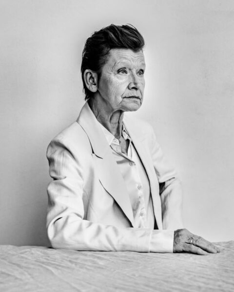 Czarno-biały portret aktorki Jadwigi Jankowskiej-Cieślak, ujęcie w stylu studyjnym na tle jasnej ściany. Ma modną, zaczesaną do góry fryzurę i intensywne spojrzenie skierowane w bok. Ubrana jest w jasną (prawdopodobnie białą lub kremową) marynarkę i koszulę o satynowym wykończeniu.